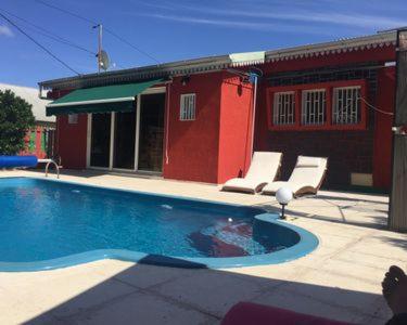 a swimming pool in front of a red building at VyvyRUN974 in Les Cocos