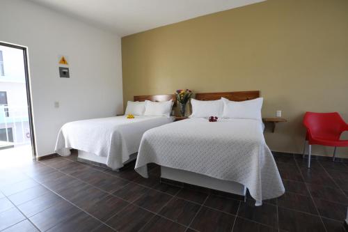 a bedroom with two beds with white sheets and a red chair at Hotel Del Mar in Barra de Navidad