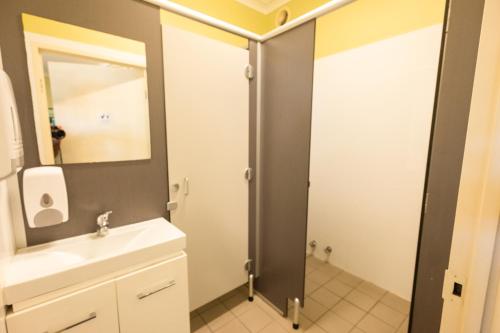 een badkamer met een wastafel en een douche met een spiegel bij YHA Newcastle Beach in Newcastle