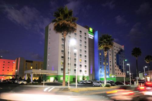 un grand bâtiment blanc avec des palmiers dans un parking dans l'établissement Holiday Inn Express & Suites Toluca Zona Aeropuerto, an IHG Hotel, à Toluca