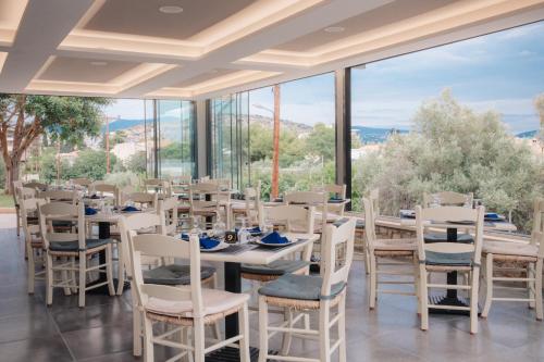 a dining room with tables and chairs and large windows at Apollon Hotel in Tolo