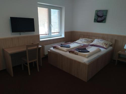 a bedroom with a bed and a desk and a television at Penzion Zátiší in Komorní Lhotka