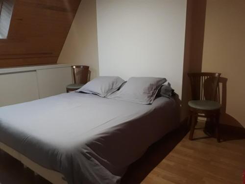 un letto con lenzuola bianche e due sedie in una stanza di les gites du grenit a La Chapelle-Neuve