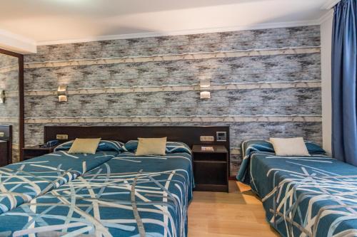 a bedroom with two beds and a brick wall at Hotel Gijon in Gijón