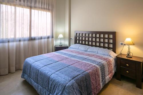 a bedroom with a bed with a blue blanket and a window at Apartamentos Turísticos La Castilleja in Córdoba