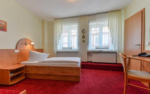 a bedroom with a bed and a desk and windows at Hotel Kirchhainer Hof in Kirchhain