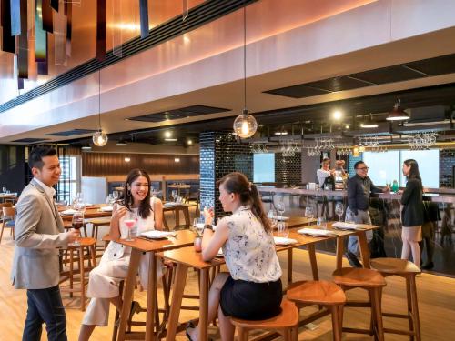 a group of people sitting at tables in a restaurant at Novotel Bangkok IMPACT in Nonthaburi