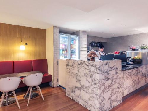 a restaurant with a counter with chairs and a person in the kitchen at Mercure Brisbane King George Square in Brisbane