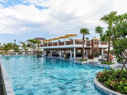 une piscine dans un complexe avec des palmiers et un bâtiment dans l'établissement Premier Village Danang Resort Managed By Accor, à Đà Nẵng