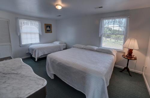 a bedroom with two beds and a lamp and two windows at Outer Banks Motel - Village Accommodations in Buxton