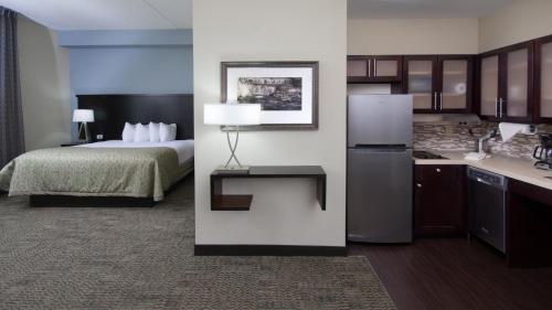 a hotel room with a bed and a kitchen with a refrigerator at Staybridge Suites Buffalo-Amherst by IHG in Amherst
