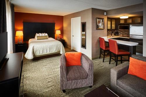 a hotel room with a bed and chairs and a kitchen at Staybridge Suites Hamilton - Downtown by IHG in Hamilton