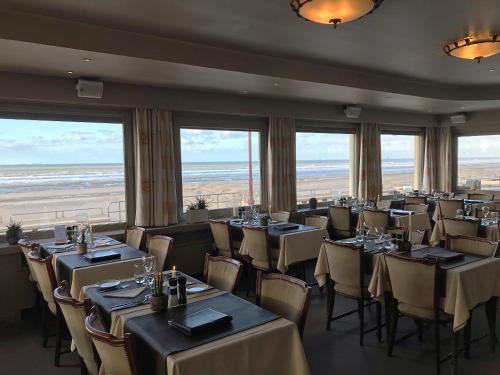 a dining room with tables and chairs and windows at Strandhotel De Haan in De Haan