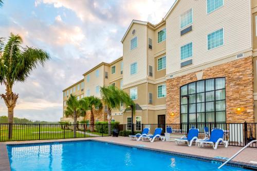 a swimming pool with blue chairs and a building at Staybridge Suites - Brownsville by IHG in Brownsville