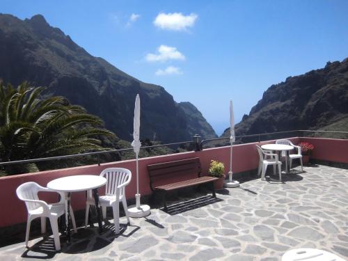 a patio with tables and chairs and a bench and mountains at Live Masca - Estudio casas morrocatana Tenerife in Masca