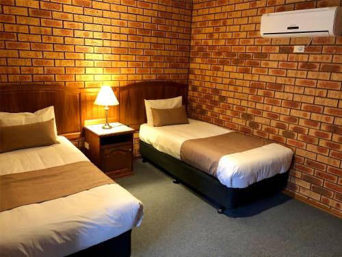 a room with two beds and a brick wall at Victoriana Motor Inn in Ballarat