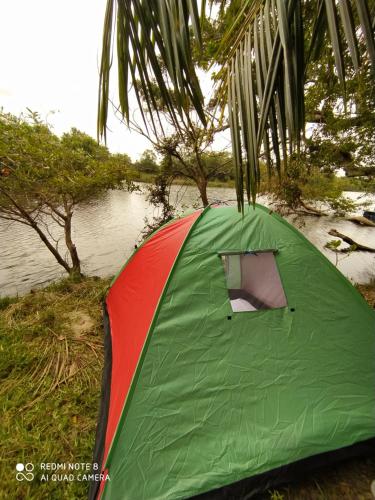 a green and red tent next to a body of water at Wilpattu Green Cabin in Achchamulai