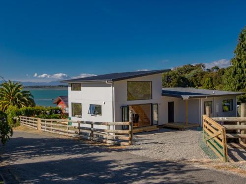 a white house with a fence and water in the background at Tapu Bay Treasure - Kaiteriteri Holiday Home in Kaiteriteri
