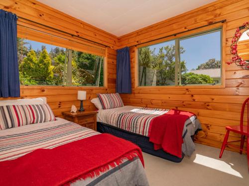 two beds in a room with wooden walls and windows at Picturesque on Paku - Tairua Holiday Home in Tairua