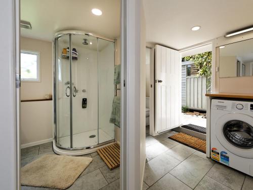 y baño con ducha y lavadora. en Surfer's Sunshine Cottage - Piha Holiday Home, en Piha