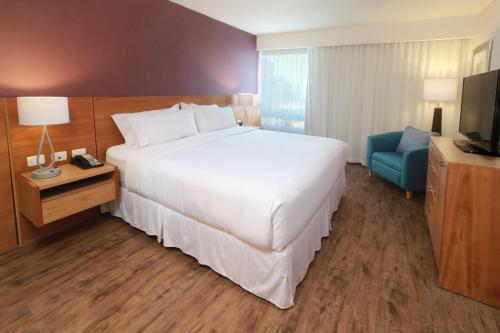 a bedroom with a large white bed and a blue chair at Staybridge Suites Guadalajara Expo by IHG in Guadalajara