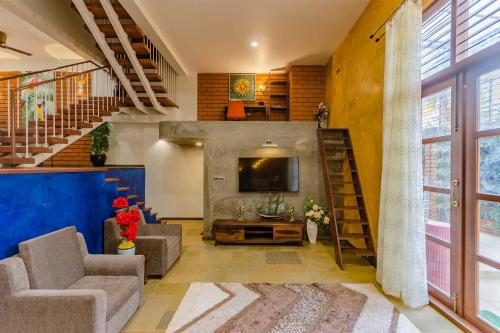 a living room with a couch and a tv and a staircase at Udhbhava Kamala by VEO - Part of StayVista in Bengaluru