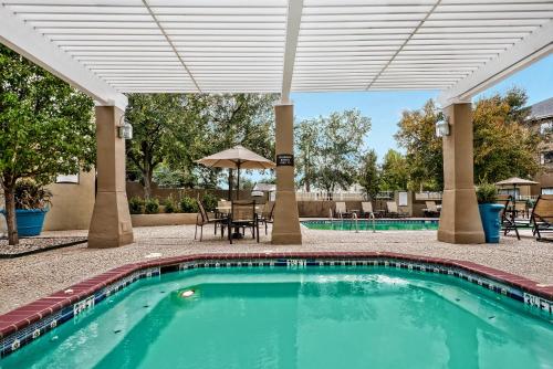 a swimming pool with an umbrella and tables and chairs at Staybridge Suites Lubbock-University Area by IHG in Lubbock