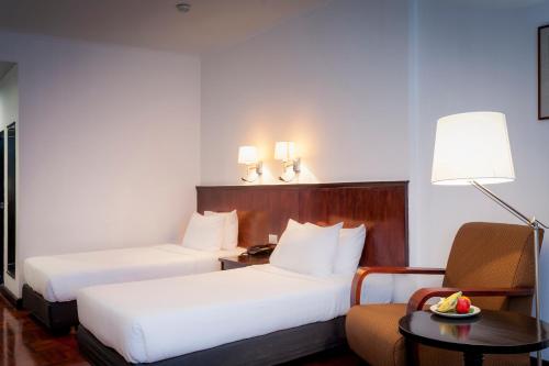 a hotel room with two beds and a chair at Le Charme Vientiane Hotel in Vientiane