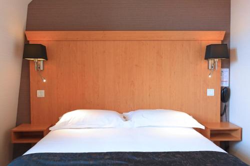 a bed with a wooden headboard with two white pillows at Hôtel L'Escale - Piscine & SPA in Escalles