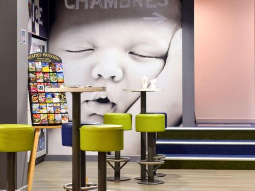 a restaurant with green chairs and a poster of a baby at ibis budget Pau Lescar in Lescar