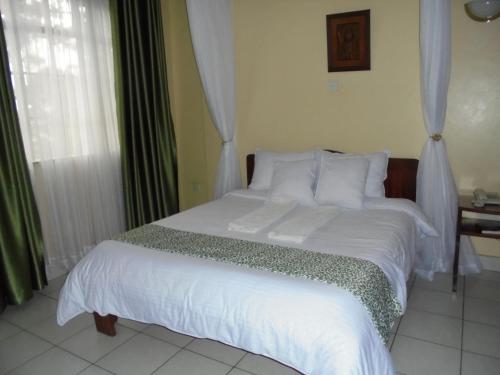 Una cama con sábanas blancas y almohadas en un dormitorio en Adventist LMS Guest House & Conference Centre en Nairobi