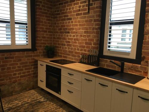 a kitchen with white cabinets and a brick wall at The Stables Dunedin in Dunedin