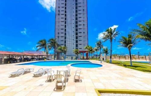 a pool with chairs and a table and a building at Apto Vista Beira Mar - Praia do Futuro a 100 mt da Praia in Fortaleza