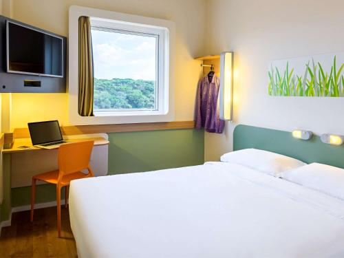 a bedroom with a bed and a desk and a window at ibis budget Curitiba Aeroporto in São José dos Pinhais