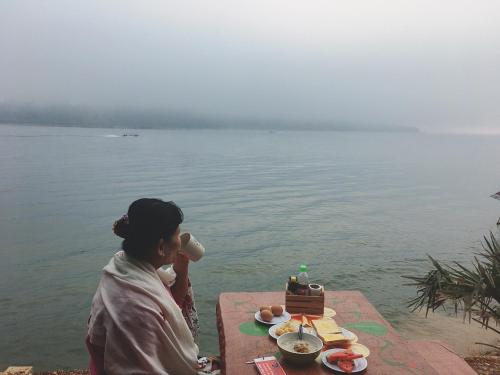 a woman sitting at a table by the water with a cake at Baan Dongsak River view in Sangkhla Buri