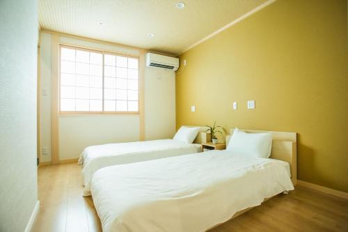 two beds in a room with yellow walls and a window at Oyado Toshi in Kyoto