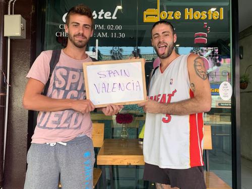 two men holding a sign in front of a store at Doze Hostel in Chiang Mai