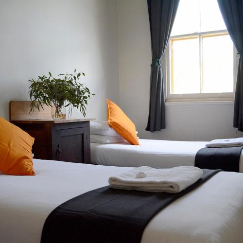 a room with three beds with orange pillows and a window at Shamrock Hotel Motel Temora in Temora