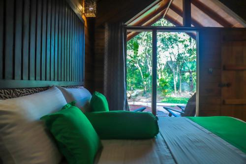 a bedroom with a bed with green pillows and a window at Palmyra Nature Resort Sigiriya in Sigiriya