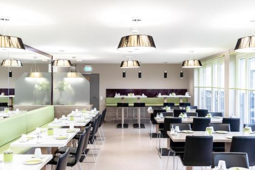 a restaurant with white tables and chairs and windows at Hotel Demas City in Munich