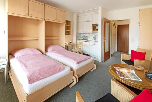 2 Betten in einem kleinen Zimmer mit einem Tisch und einer Küche in der Unterkunft Sylt - Haus Christianenhöhe - App 29 in Westerland