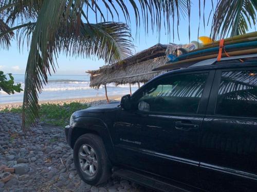 a black truck parked on a beach with a surfboard on top at Pelicano Surf Camp in La Libertad