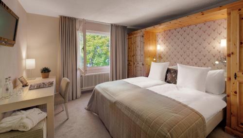 a bedroom with a bed and a desk and a window at Morosani Posthotel in Davos