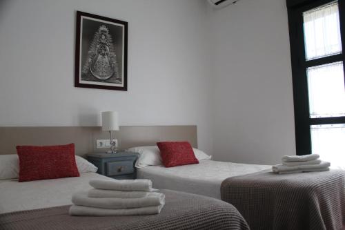 エル・ロシオにあるApartamentos Peregrinosの白いシーツと赤い枕が備わるベッド2台が備わる客室です。