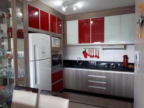 Il comprend une cuisine équipée de placards rouges et d'un réfrigérateur blanc. dans l'établissement 100m da Praia - Novo, amplo e com 4 camas de casal, à Porto Belo