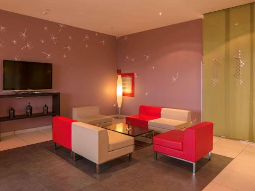 a living room with red and white chairs and a tv at Ibis Constantine in Constantine