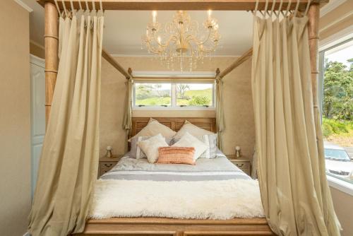 a bedroom with a canopy bed with a chandelier at ONEPU MOANA RETREAT Holiday Home in Opononi