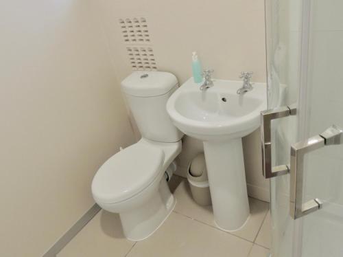 a white bathroom with a toilet and a sink at La Mer Guesthouse in Port Elizabeth