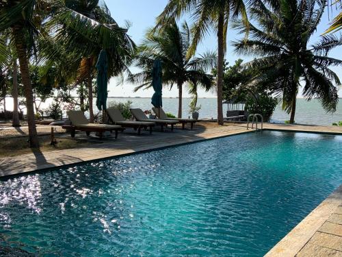 a swimming pool with palm trees and chairs and the ocean at Villa Sethawadi Hotel and Kitesurf Centre in Kalpitiya