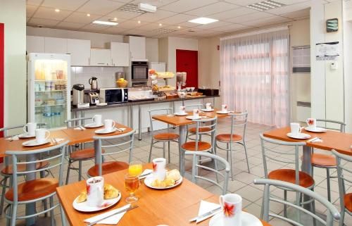 un restaurant avec des tables et des chaises en bois et une cuisine dans l'établissement Séjours & Affaires Nantes La Beaujoire, à Nantes